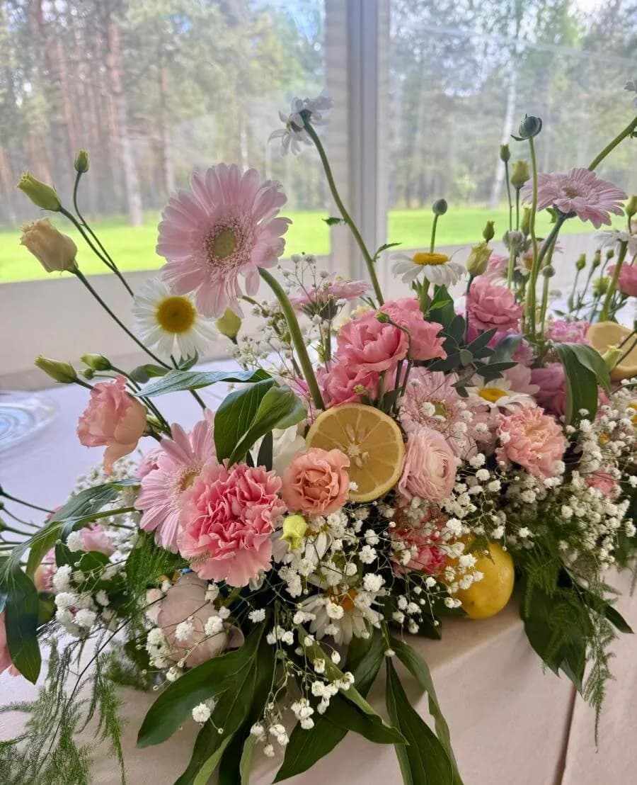 Kompozycja z różowych gerber, goździków i gipsówki z plastrami cytryny przy oknie