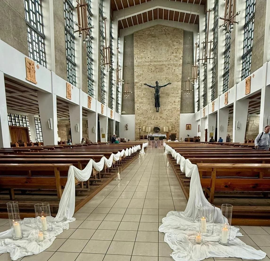 Nawa kościoła z białą tkaniną udrapowaną przy ławkach i świecami na posadzce