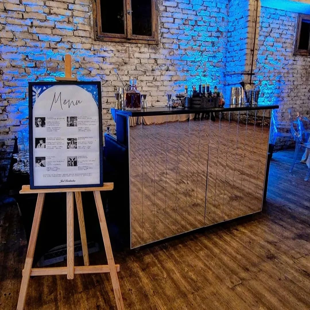 Stanowisko barowe z lustrzanym frontem przy ceglanej ścianie w niebieskim świetle i tablica z menu koktajli