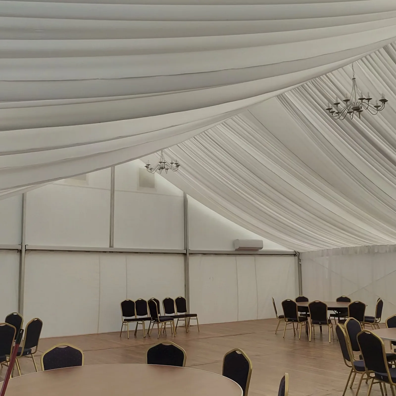Garden pavilion the day before the wedding: white fabric and chandeliers under the ceiling, round tables without tablecloths and navy blue chairs without covers