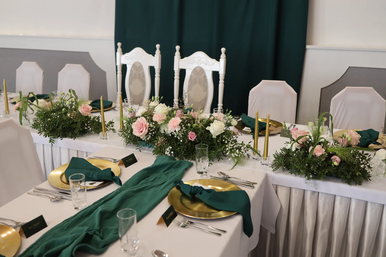 Low compositions of roses, carnations and gypsophila on the couple's table, next to gold candles, gold plates and green napkins