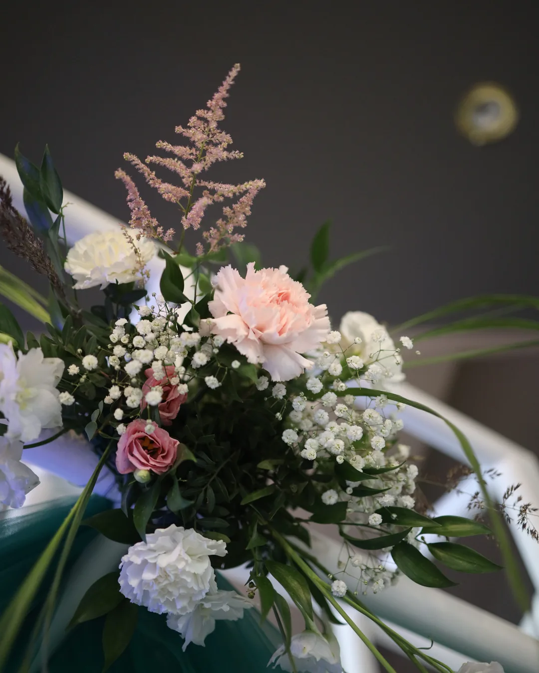 Flowers on the entrance gate: pink astilbe, carnations, eustoma and gypsophila with greenery on the background of green tulle