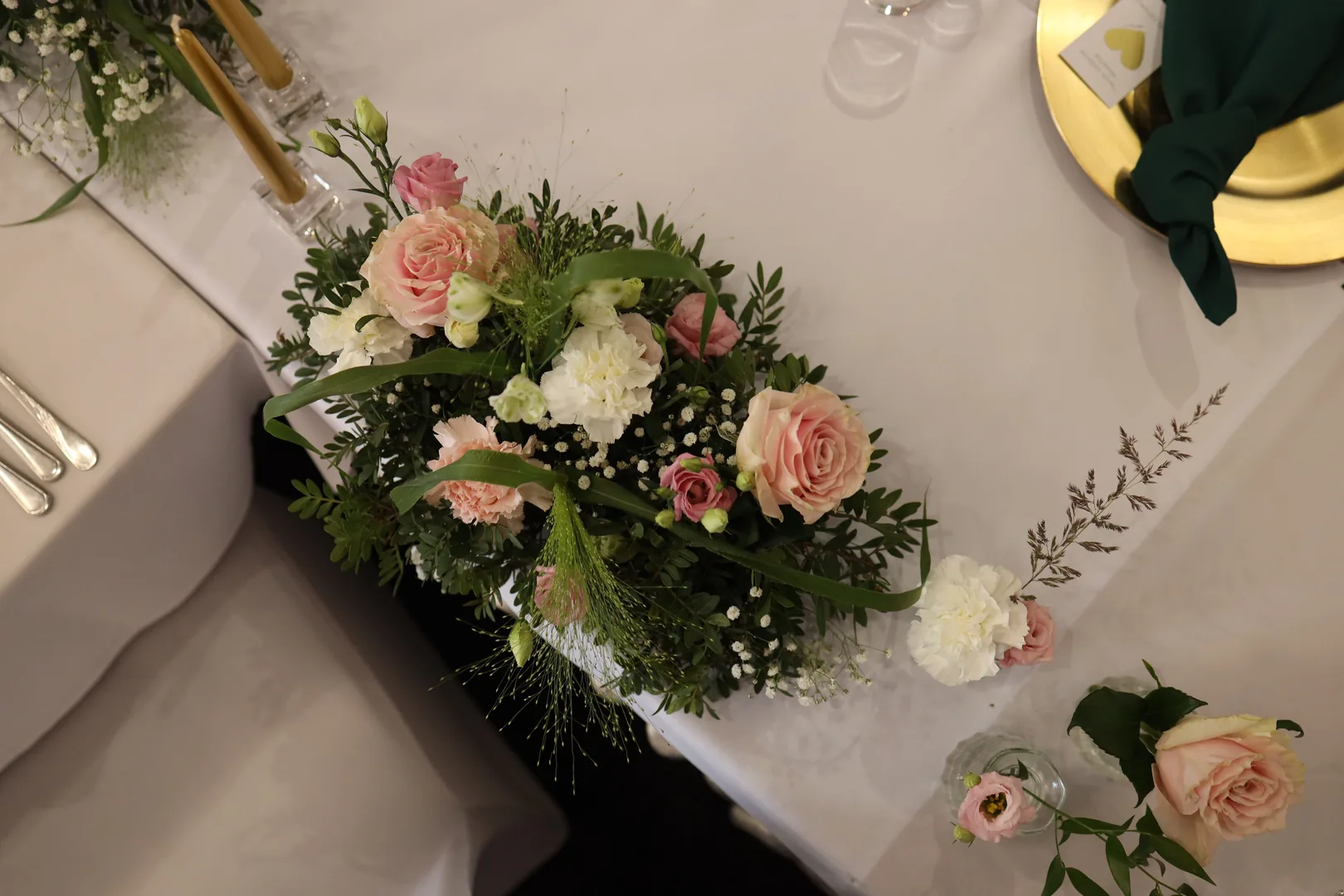 A low composition of pink roses, white carnations, eustoma and gypsophila seen from above, next to it are glass vases with single flowers