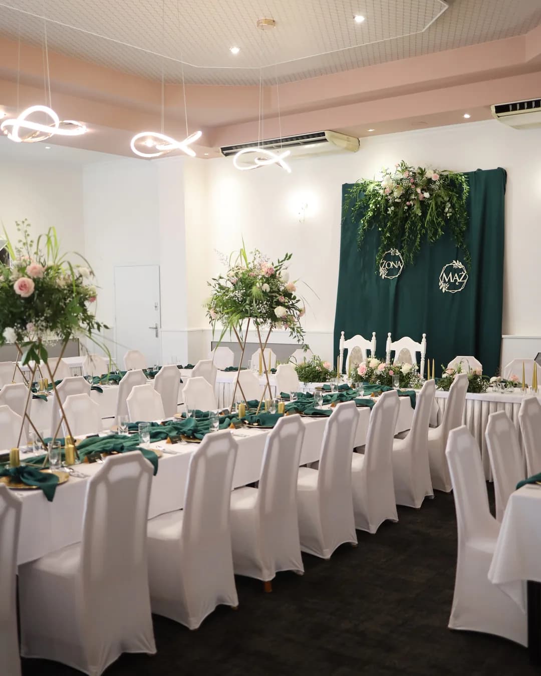 The room on the side: chairs with white covers, tall compositions on golden stands and a bottle-green wall behind the couple's table