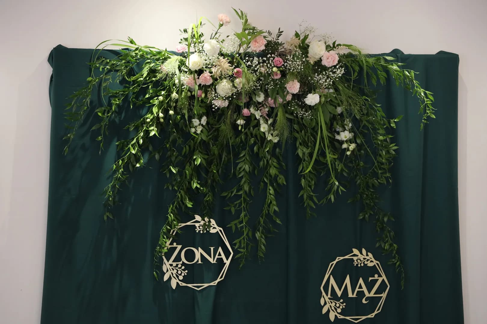 Bottle green fabric behind the couple's table with a cascading garland of roses, carnations and gypsophila and gold inscriptions "Wife" and "Husband"