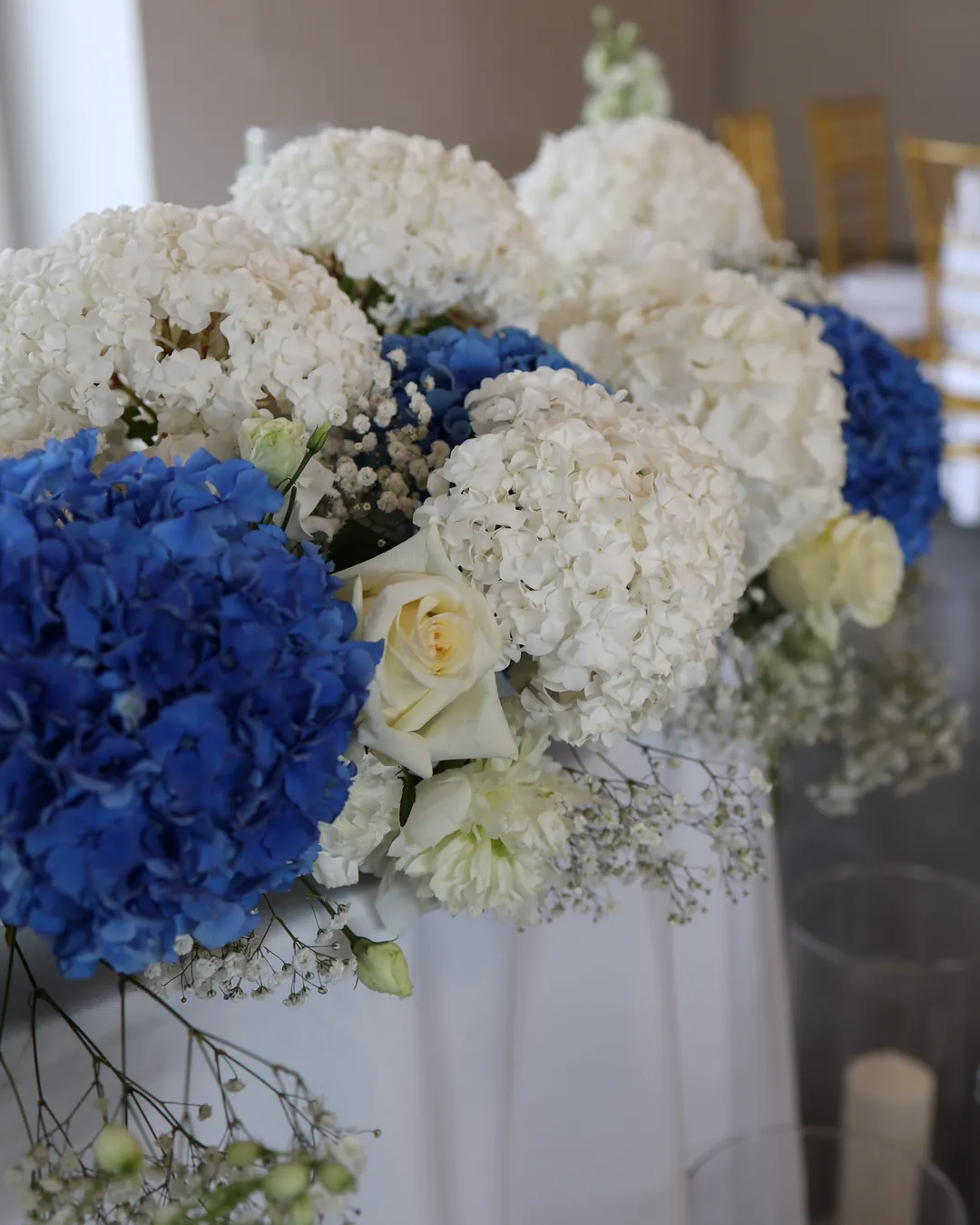 Close-up low composition on the couple's table: white and blue hydrangeas, white roses, eustoma and gypsophila