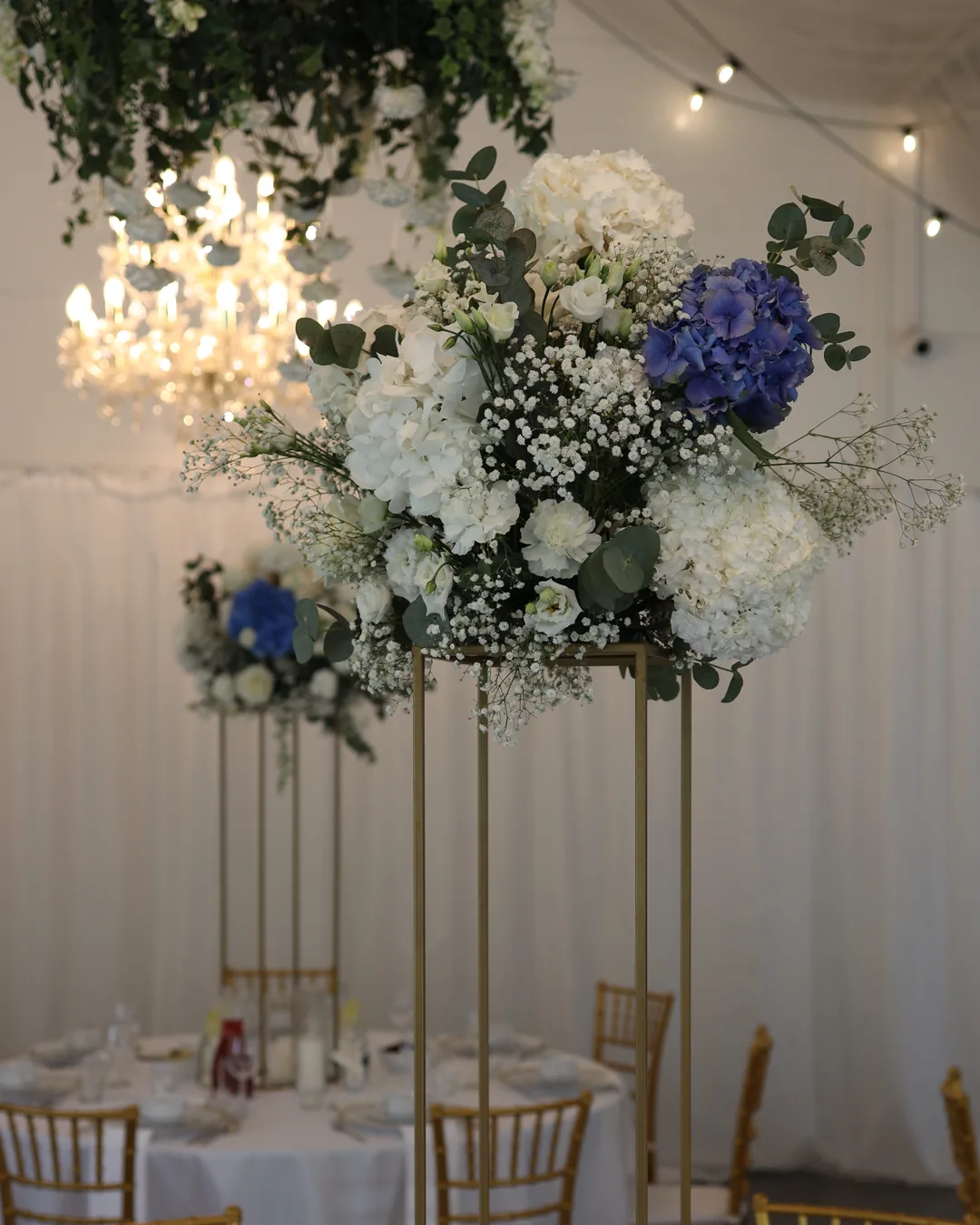 Close shot of an arrangement of white and blue hydrangea, eustoma, carnations, gypsophila and eucalyptus on a golden flower stand