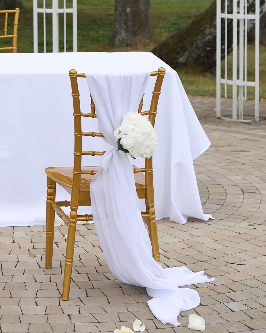 The couple's golden chair at the ceremony table decorated with white chiffon tied in a bow and a white hydrangea bouquet