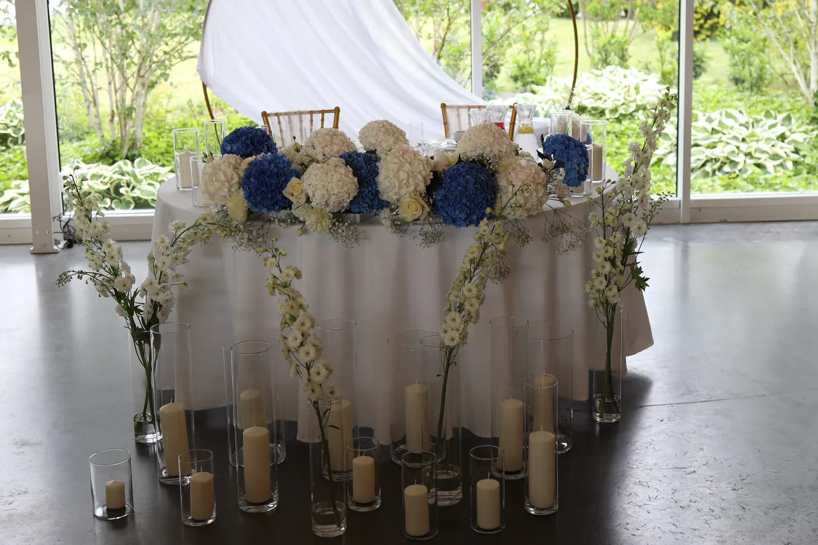 The bride and groom's table with an elongated composition of white and blue hydrangeas, white delphinium and candles in glass cylinders
