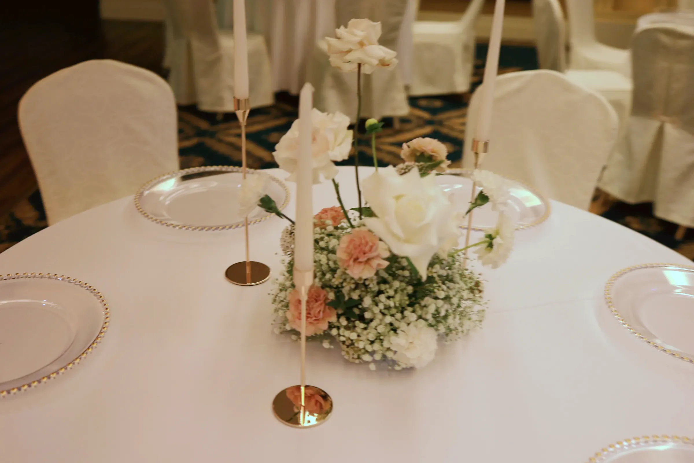Low composition with white rose, peach carnations and gypsophila cloud between two candles in golden candlesticks