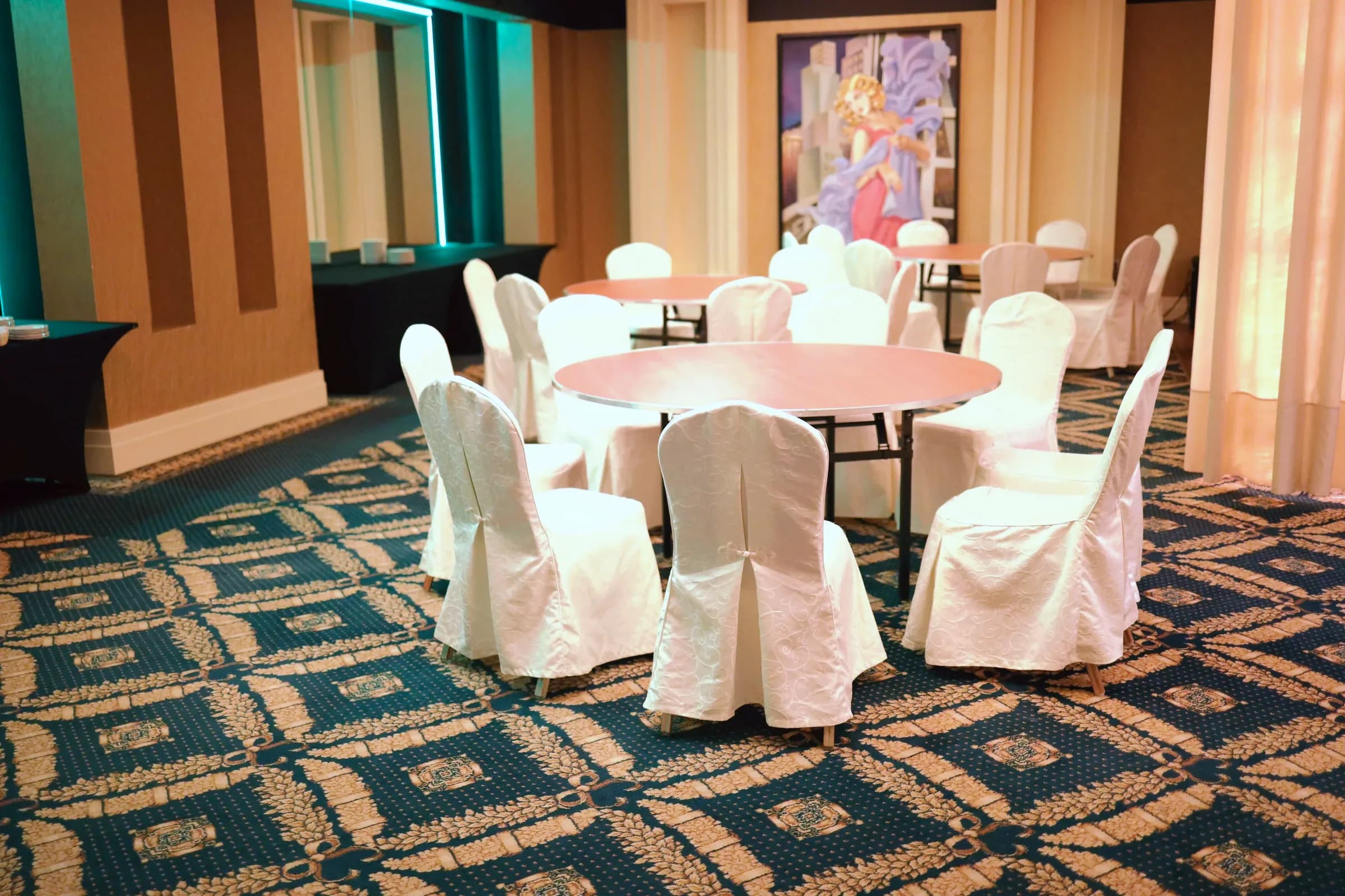 Hotel room before installation of decorations: round tables without tablecloths, chairs with white covers and patterned carpet