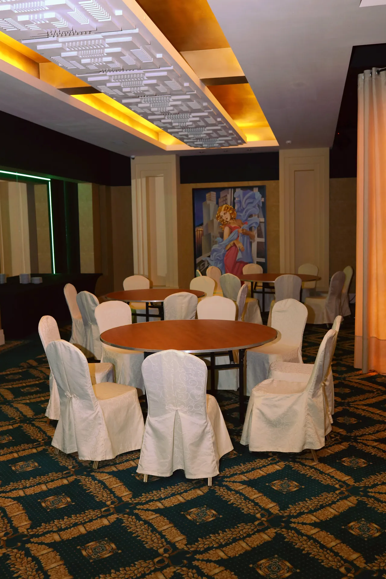 Empty room before installation: round tables without tablecloths, chairs with white covers, decorative ceiling and a painting on the wall