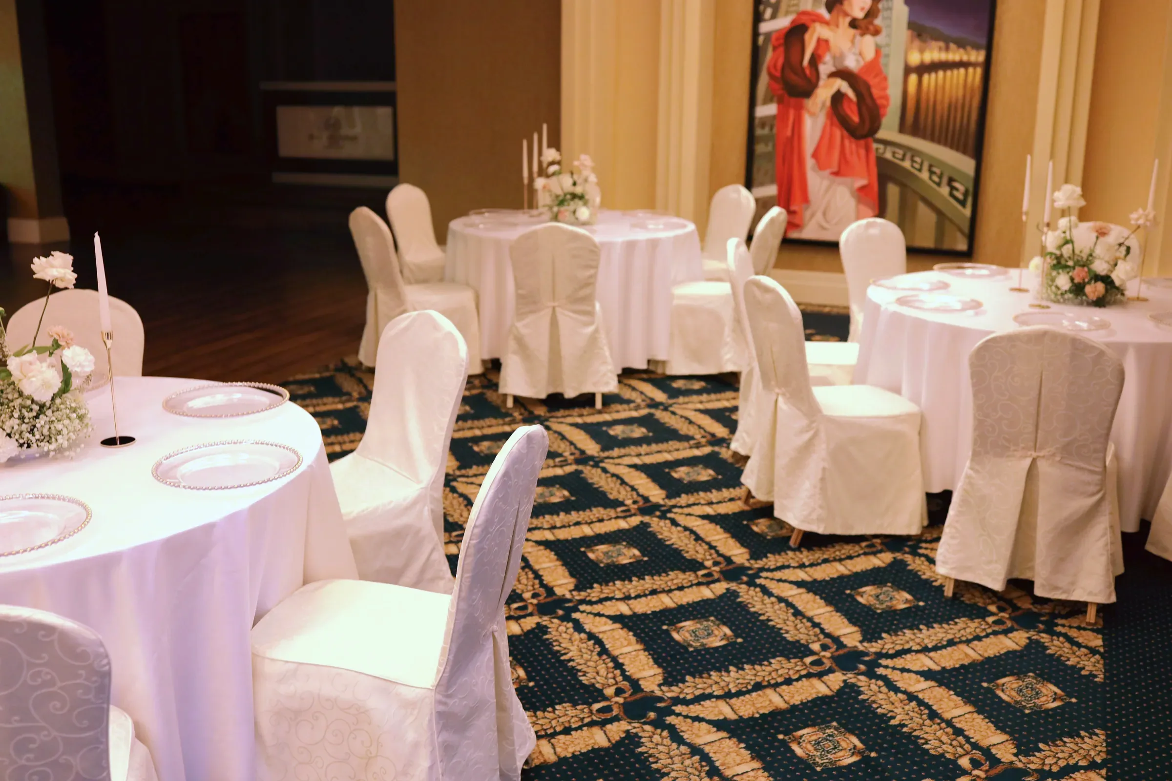 A room in the Faltom Hotel with round tables with light tablecloths, chairs with covers and low compositions with candles