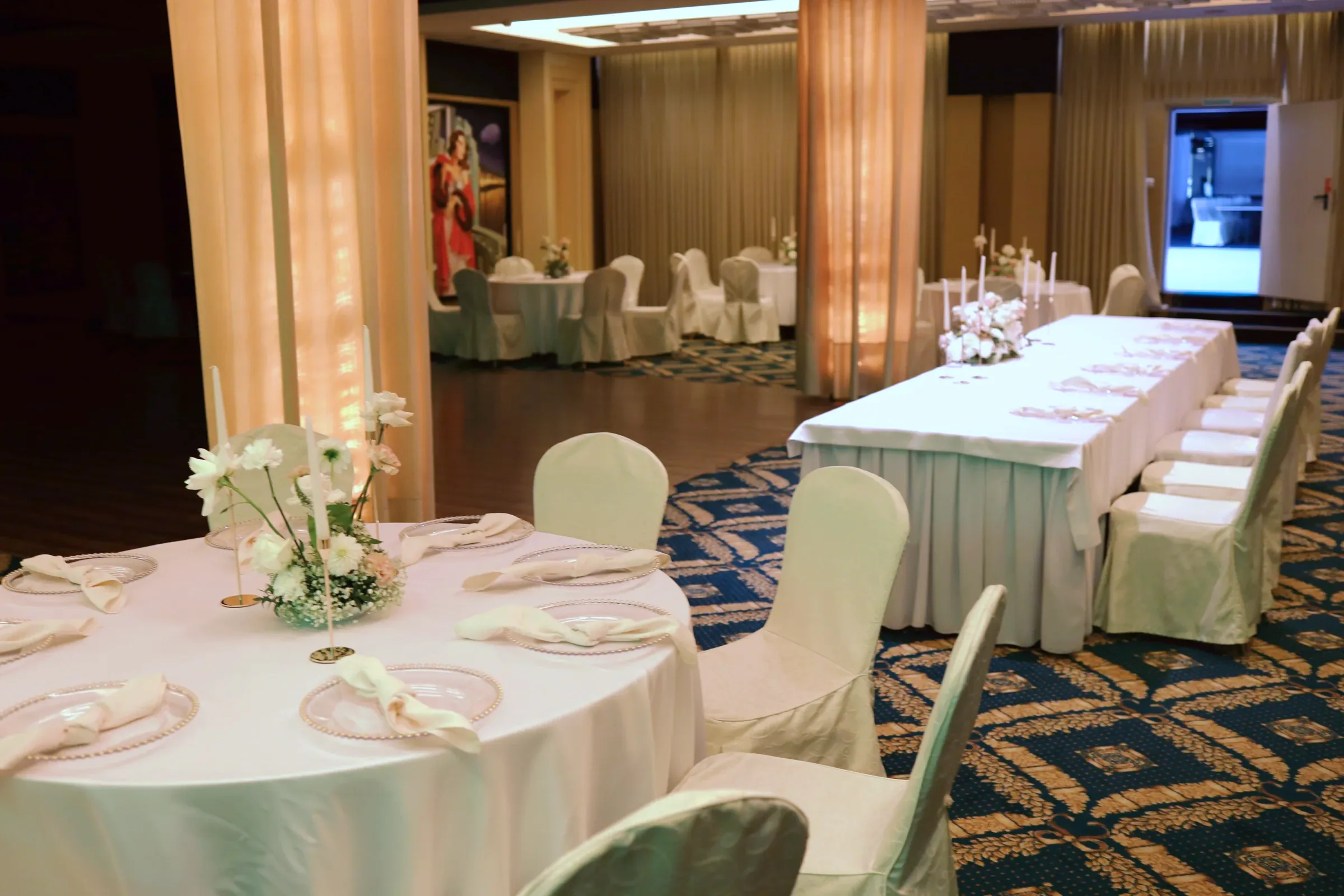 Decorated wedding hall with round tables, long table of the bride and groom and illuminated columns in warm light
