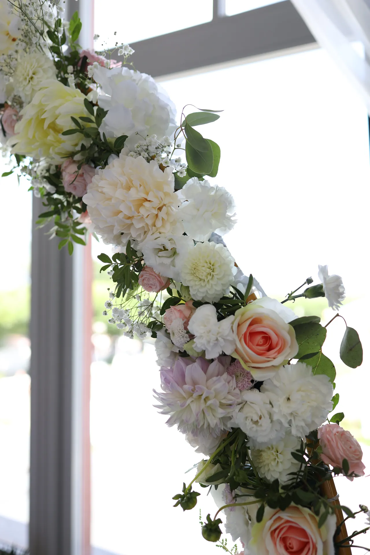 A close-up of a fragment of the hoop: white and cream flowers, pink roses and greenery against the background of a bright window