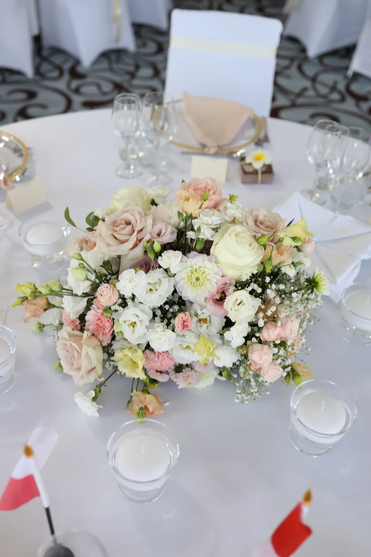 A low, round composition of roses and white flowers in the center of the table, with candles in glass covers around it