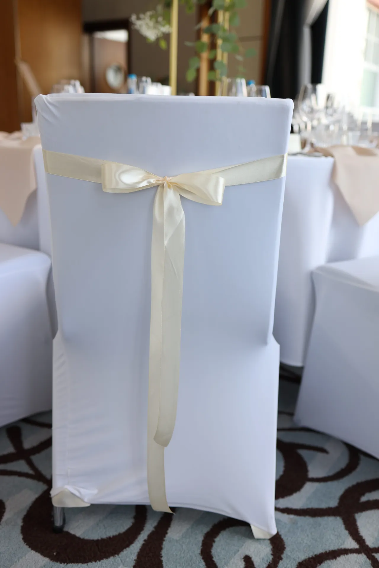 A white chair cover tied with a cream satin ribbon with a bow, a patterned carpet in the background