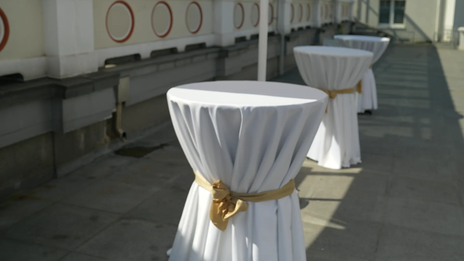 High cocktail tables in white covers with gold bows on the terrace next to the ballroom