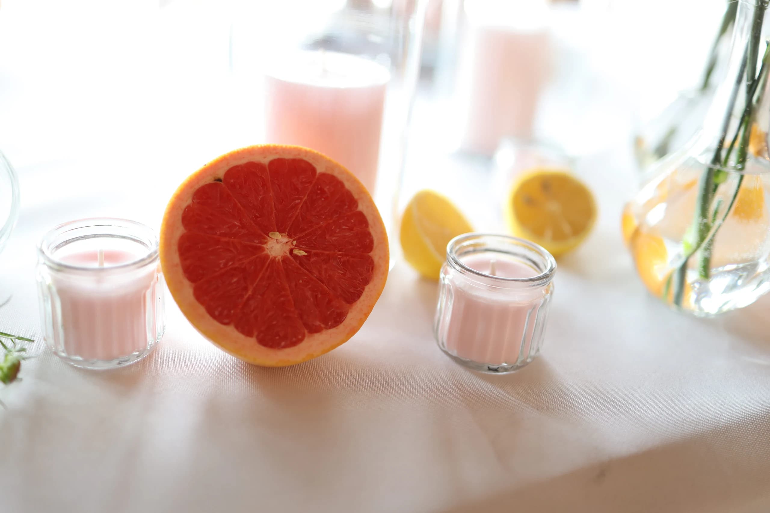 Half a grapefruit between two small pink candles in fluted jars, behind them half lemons and a pink candle