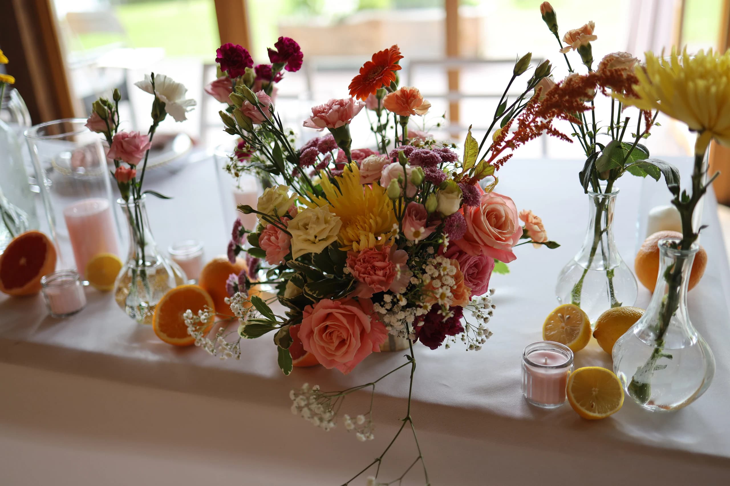 Lush composition: peach and pink roses, yellow spider chrysanthemum, orange gerbera, burgundy carnations and gypsophila, next to citrus fruits