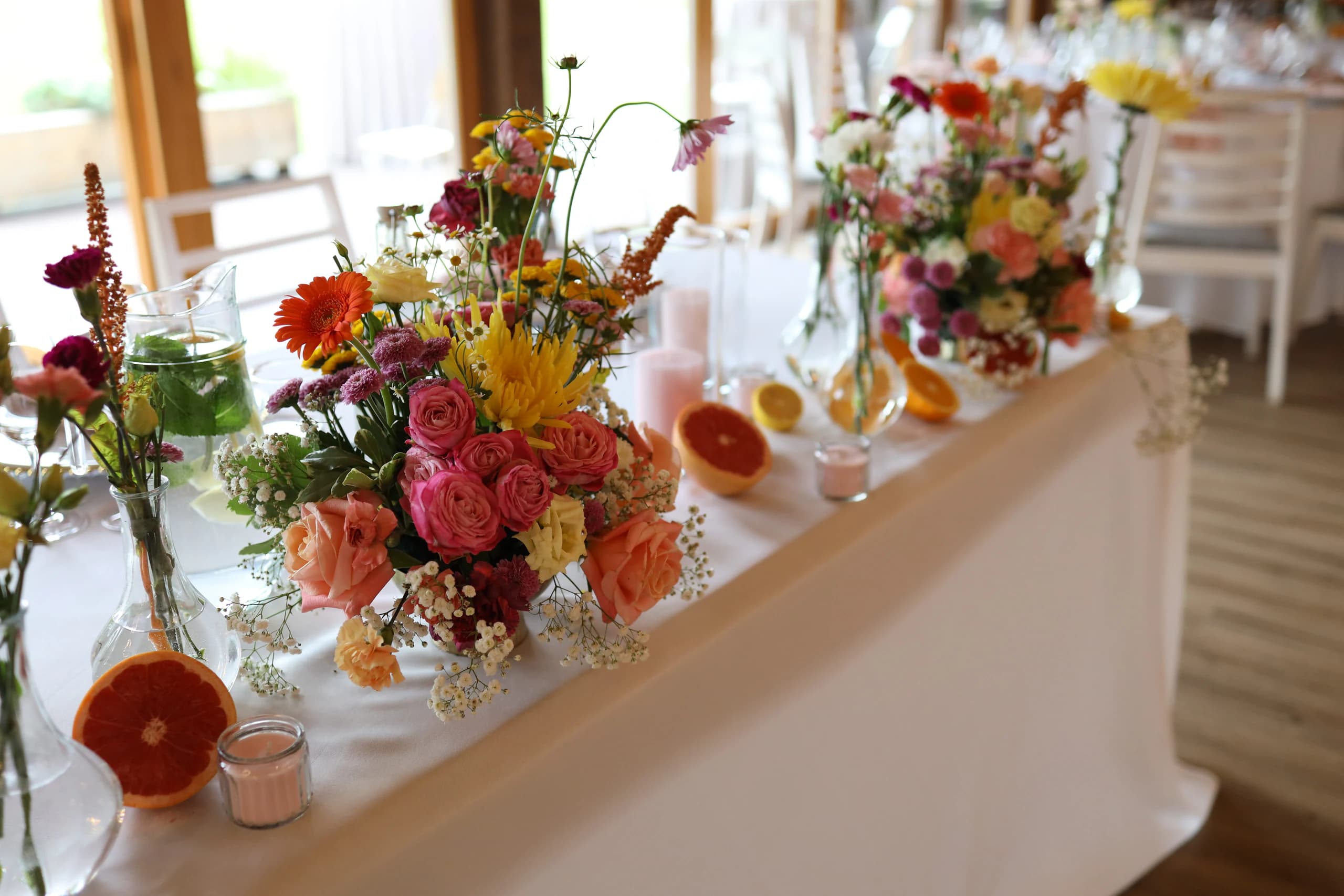Rectangular table on the side: two lush compositions, vases with flowers, a jug with mint, grapefruit halves and pink candles in glass