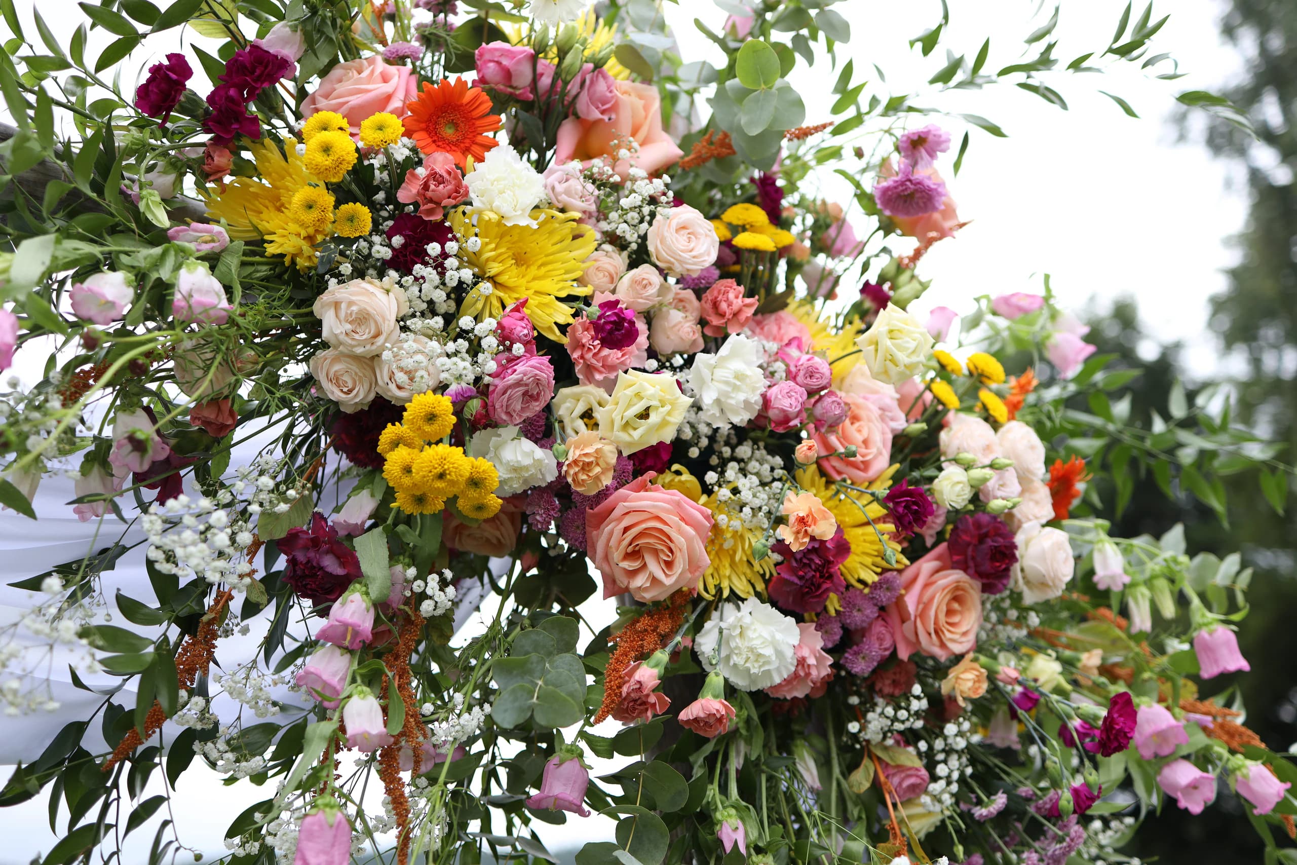 Flowers on the arch close up: peach and pink roses, orange gerbera, yellow chrysanthemums, burgundy and white carnations, cream eustomas