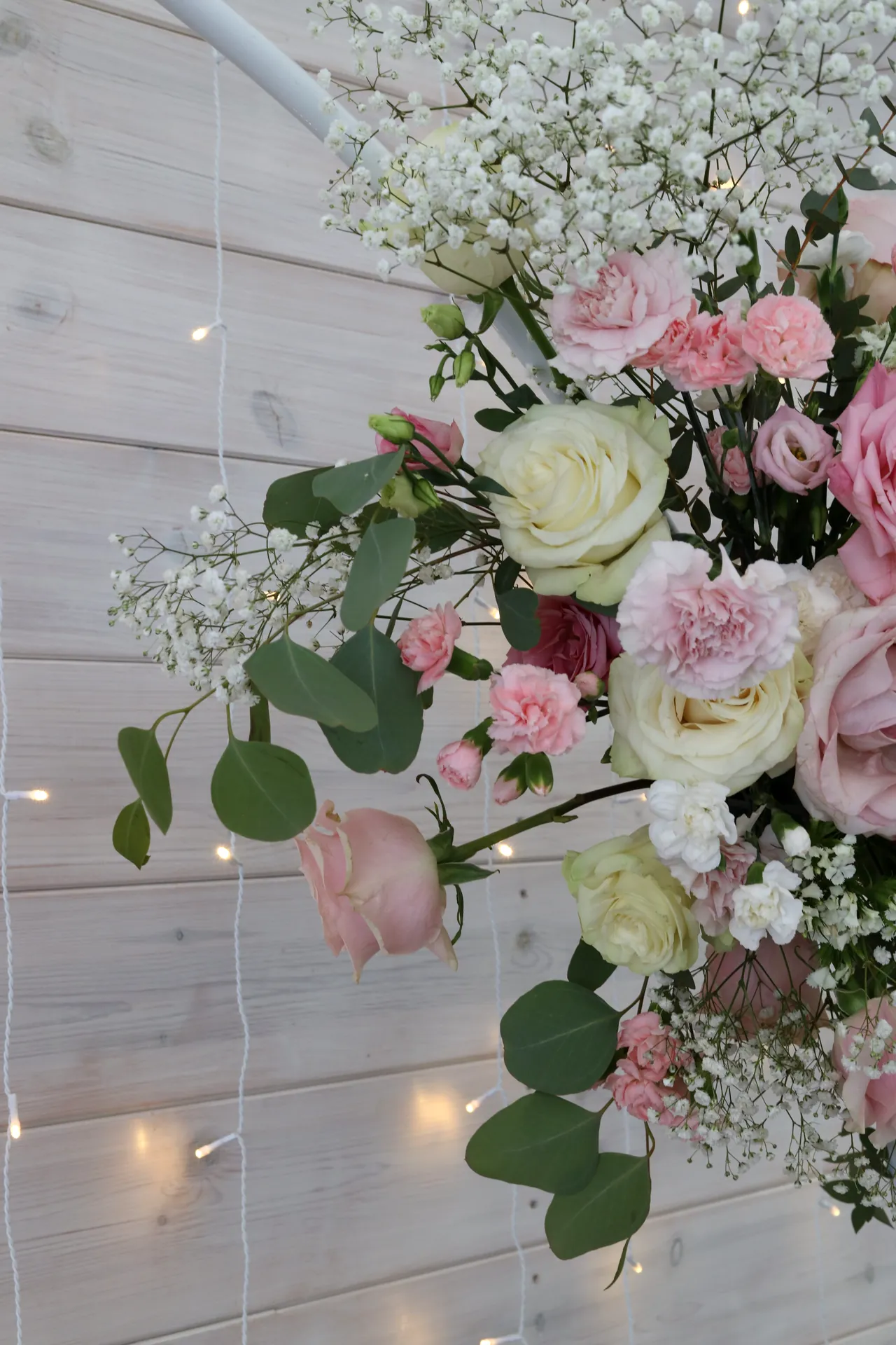 White rim with cream roses, pink carnations, gypsophila and eucalyptus on the background of boards and lights