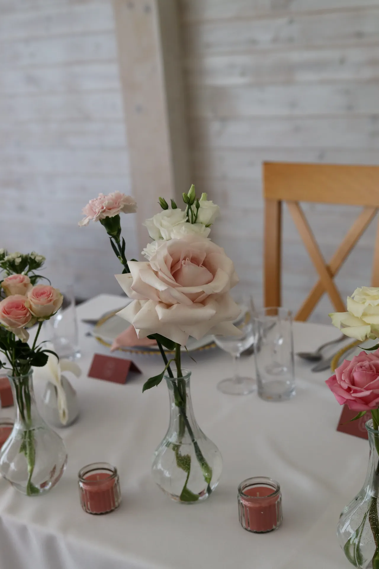 A light pink rose in a glass vase on the guests' table, and next to it there are sprigs of small roses and pink candlesticks