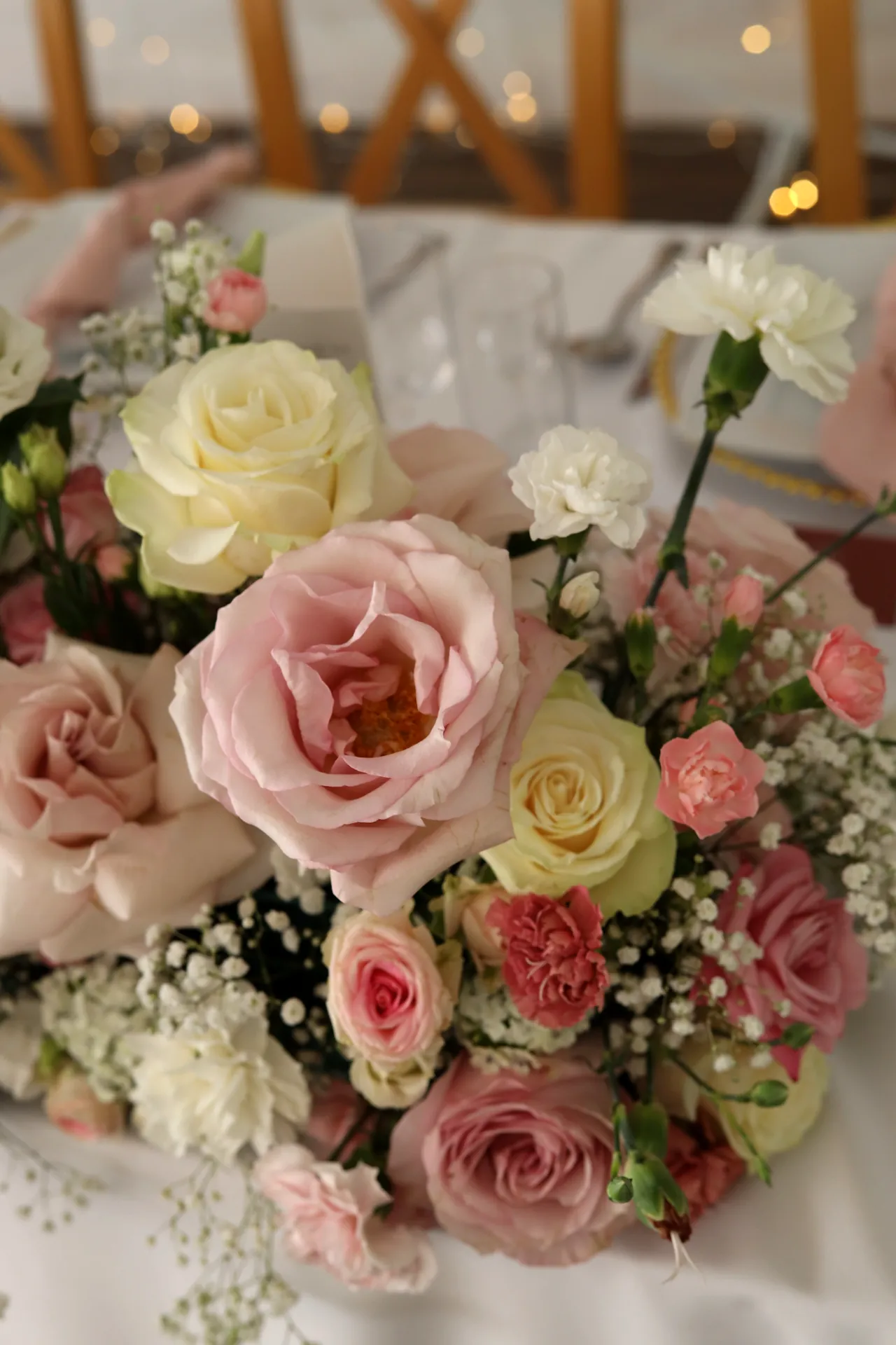 Lush composition on the bride and groom's table with pink and cream roses, carnations and white gypsophila close-up