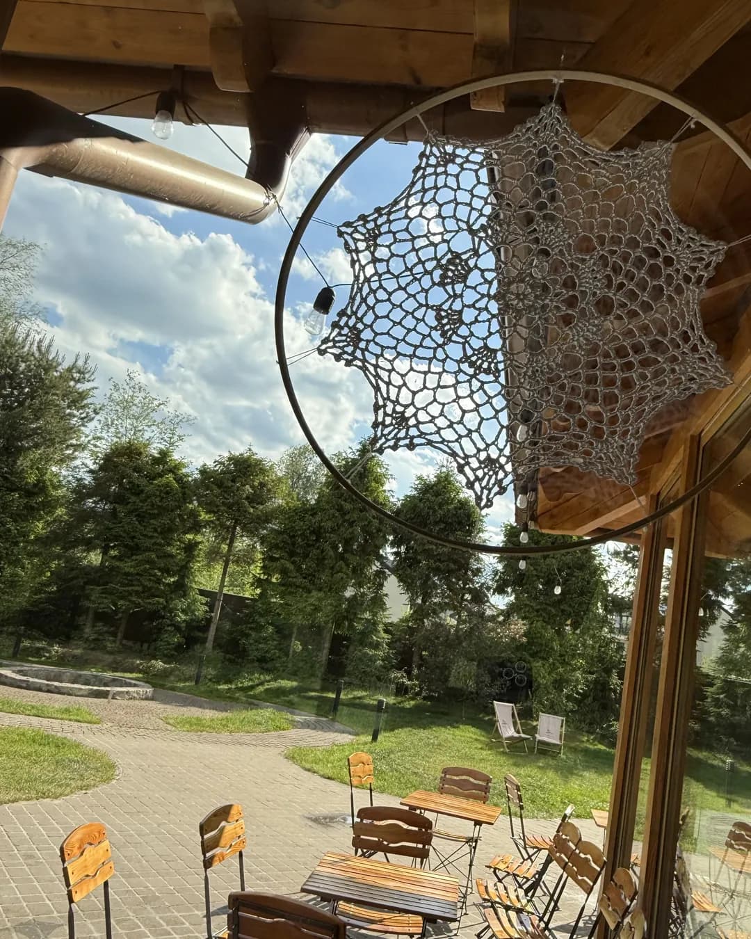 A lace dream catcher on a wooden terrace, behind it a garden with a lawn, trees and garden chairs