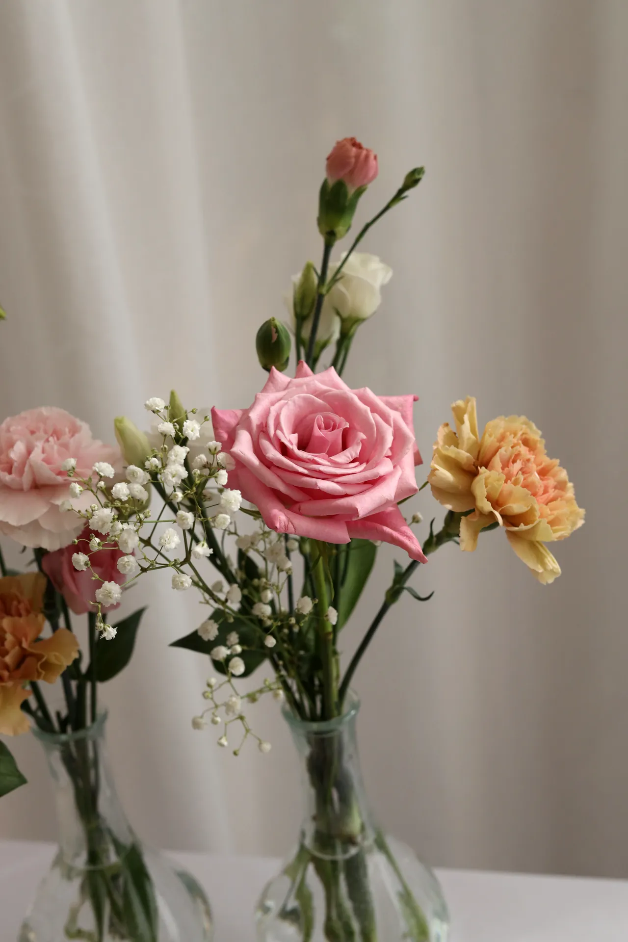 Loose bouquets in glass vases: pink rose, peach carnation, gypsophila and carnation buds