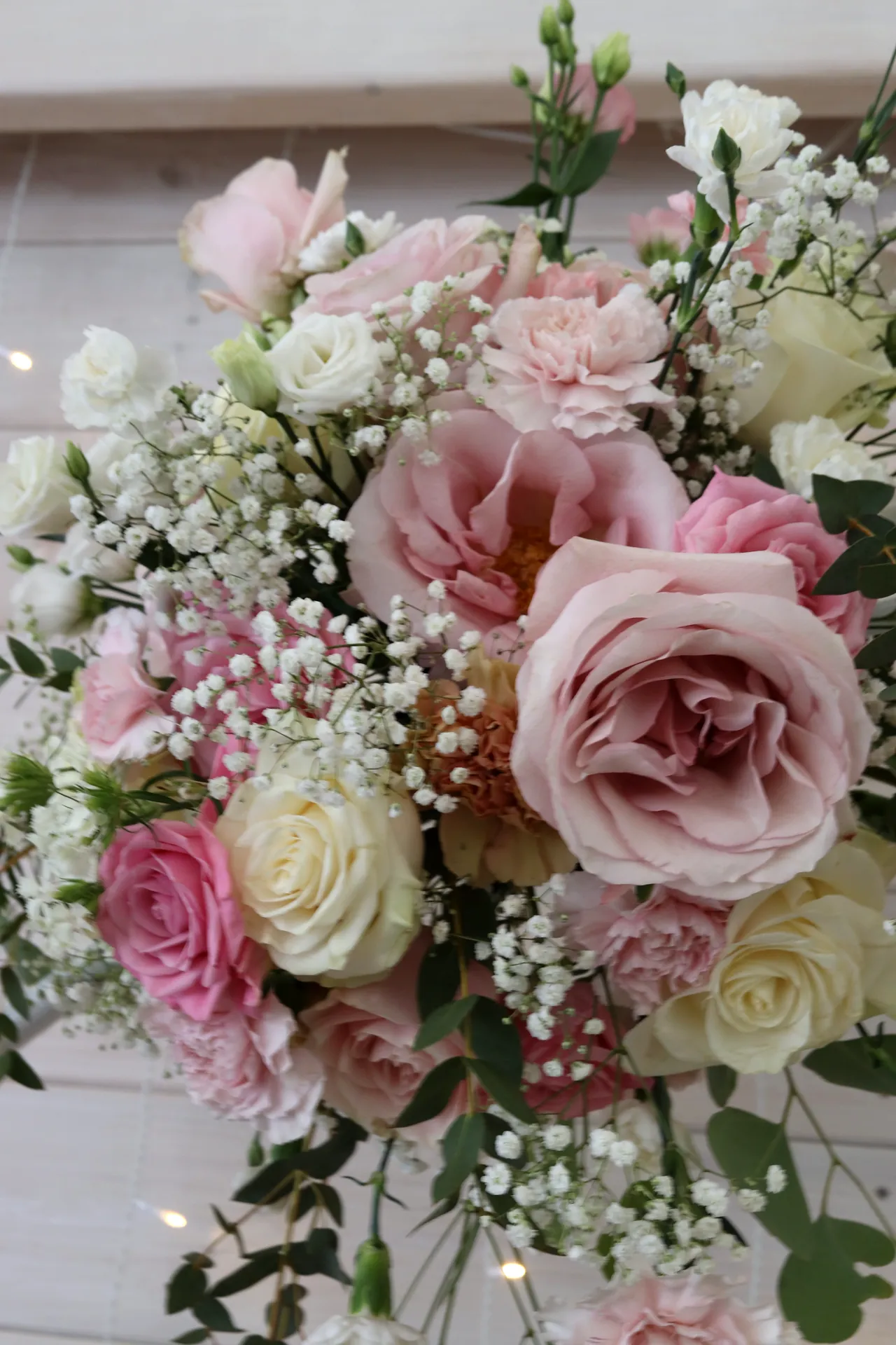 Powder pink and cream roses interwoven with white gypsophila and greenery, composition on a rim close-up