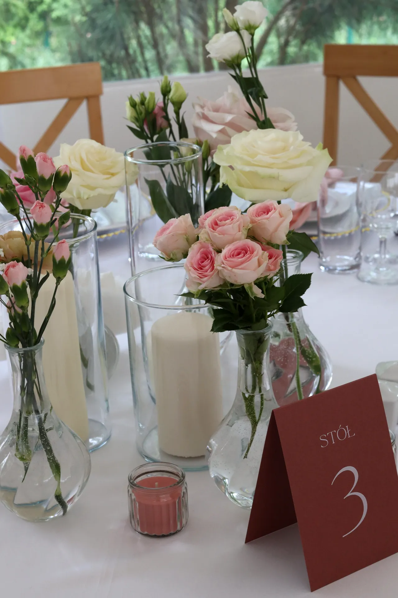 Guest table with roses, cream rose and candle in glass, next to it a burgundy table number and a pink candlestick