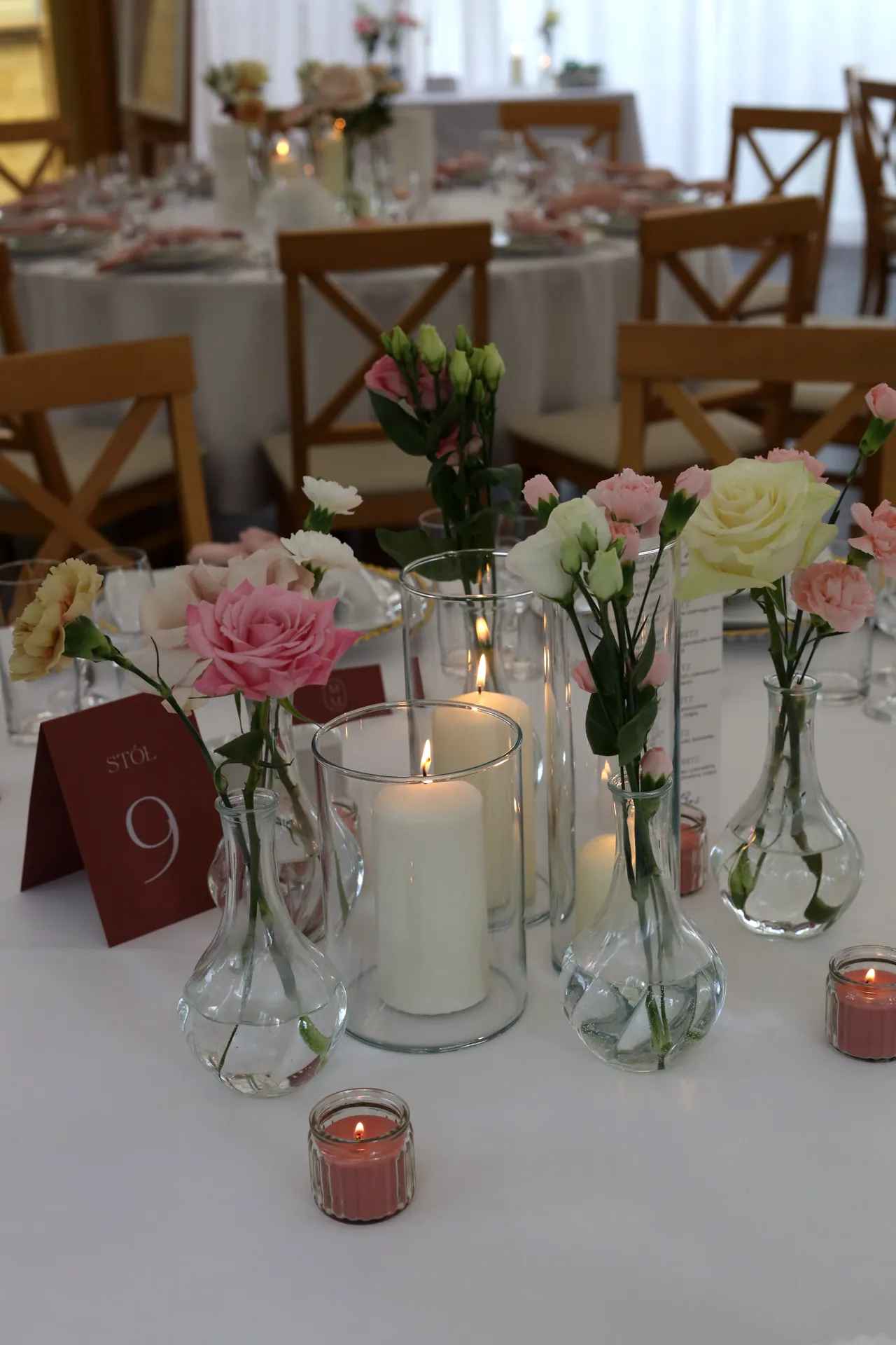 Candles in glass cylinders and vases with pink rose and bright flowers on the guests' table next to the table number