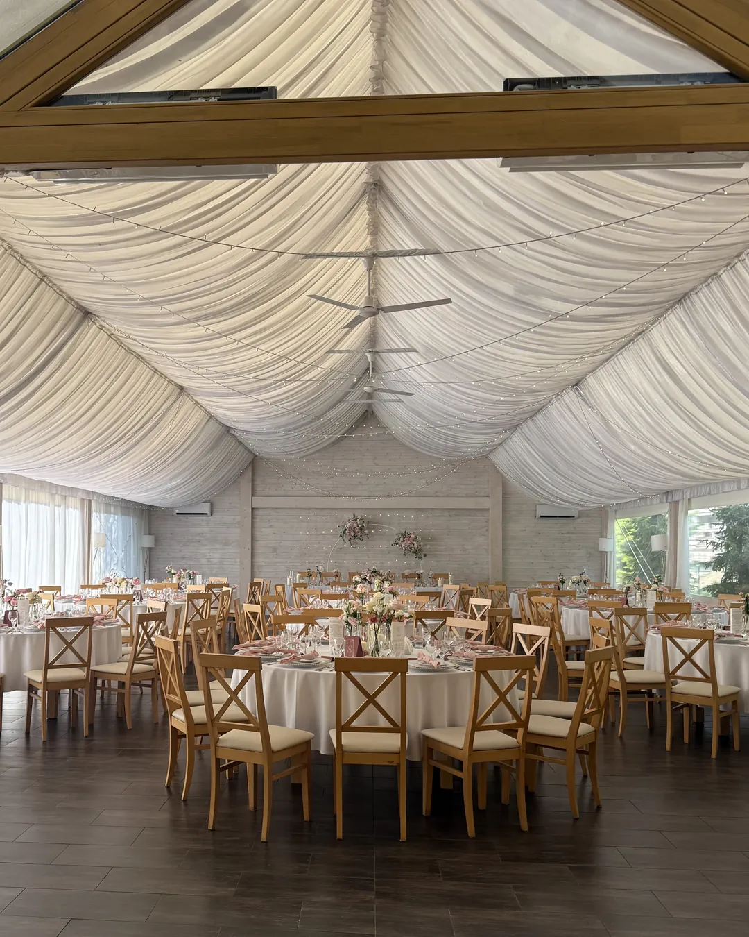 The view from the entrance to the hall under the white draped ceiling, rows of round tables and the bride and groom's table in the background
