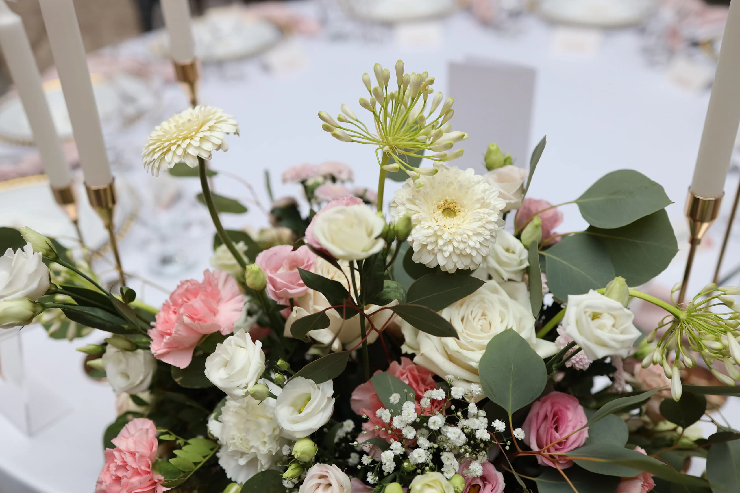 Close-up of the composition: cream gerberas, agapanthus buds, pink carnations, white and pink eustomas, white roses, gypsophila and eucalyptus, white candles on the sides