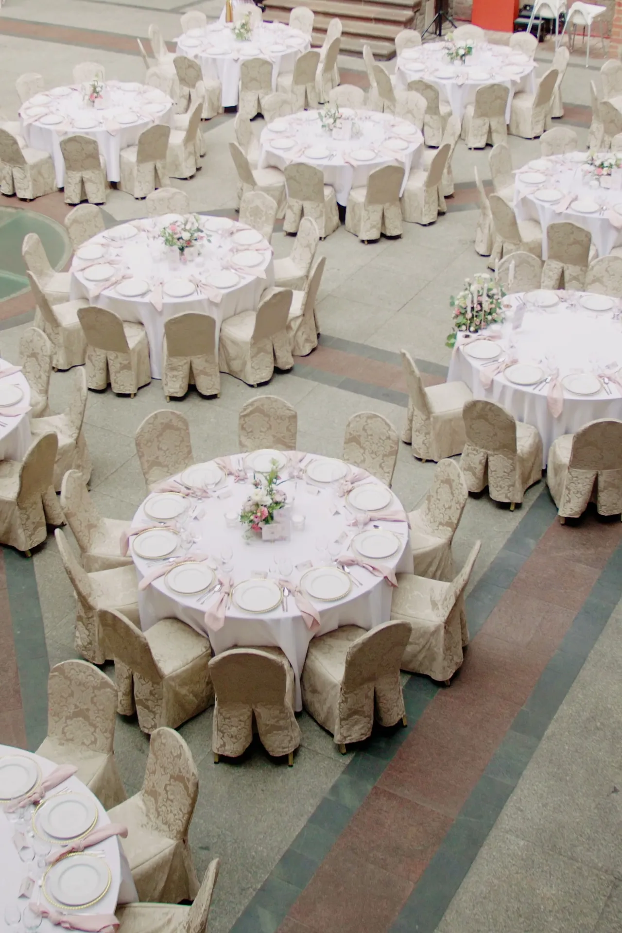 Top view of round tables in white tablecloths with low compositions in the middle and chairs in beige covers