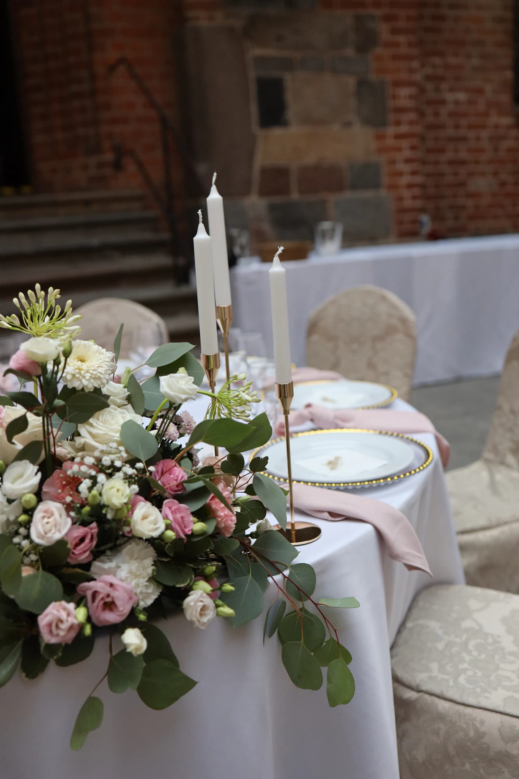 Table number 1 from the side: composition with eucalyptus in the foreground, three white candles in gold candlesticks and two place settings, stone stairs in the background