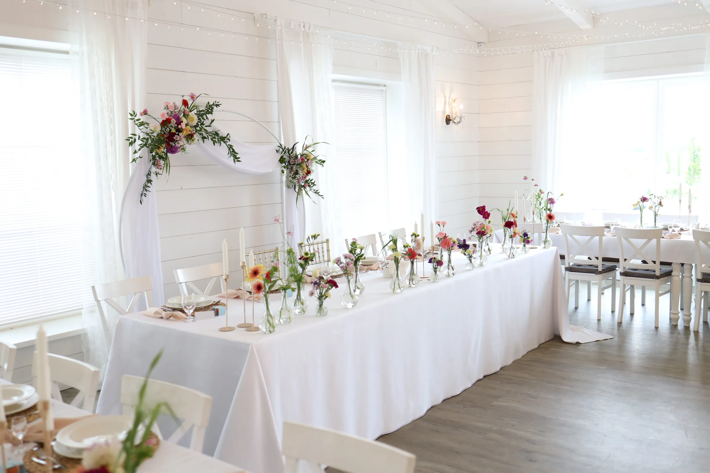 Couple's table with a row of glass vases with wild flowers and white candles, behind it a circle with tulle and flowers