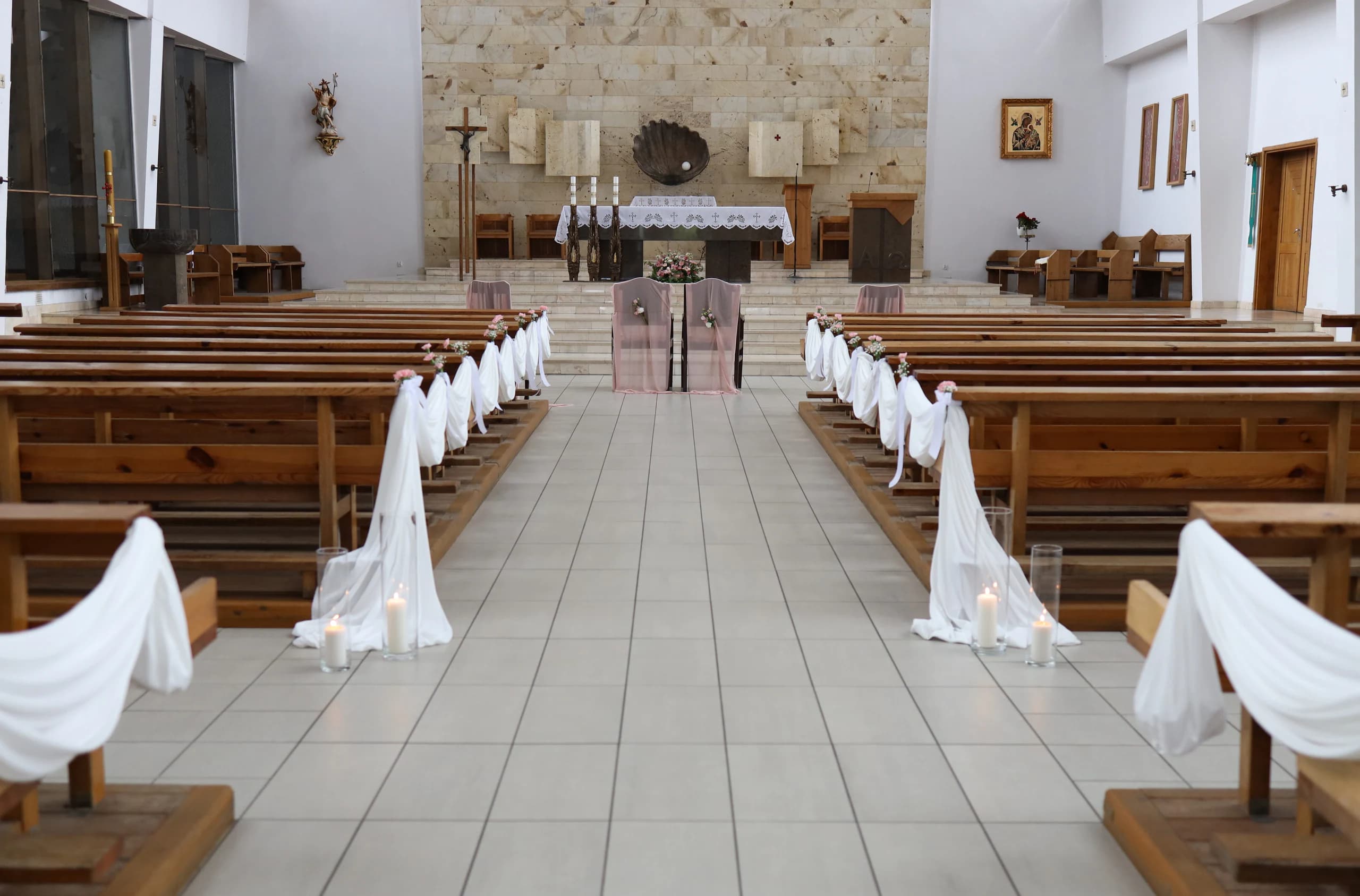 Church interior: white fabric in waves along the benches, white bows and pink bouquets, two chairs in pink fabric in front of the altar