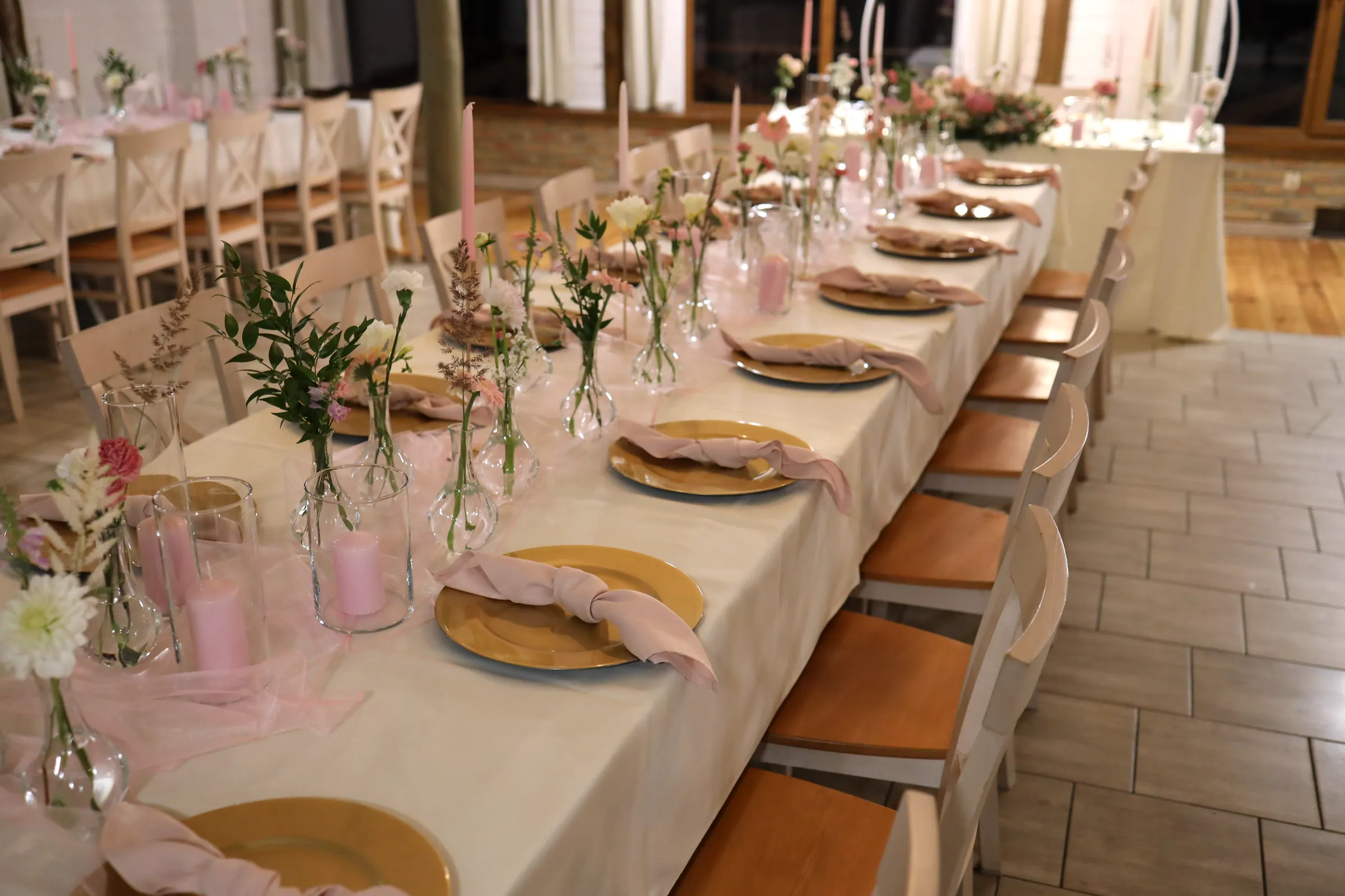 A long table of guests with vases, pink candles and gold plates leads the eye to the bride and groom's table with a flower arrangement