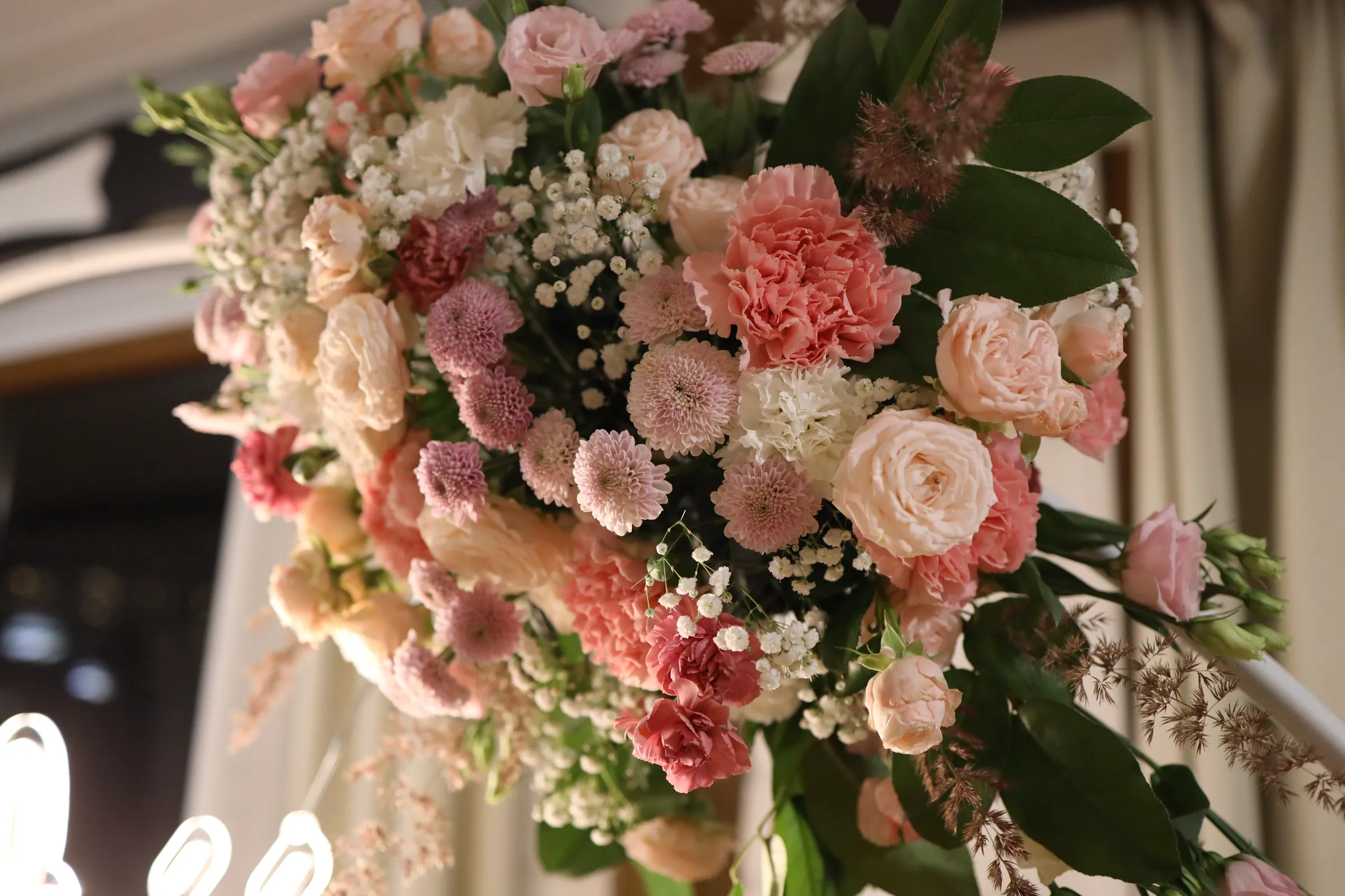 Close-up composition on a white rim: coral carnations, spray roses, tiny pink chrysanthemums, gypsophila and leaves