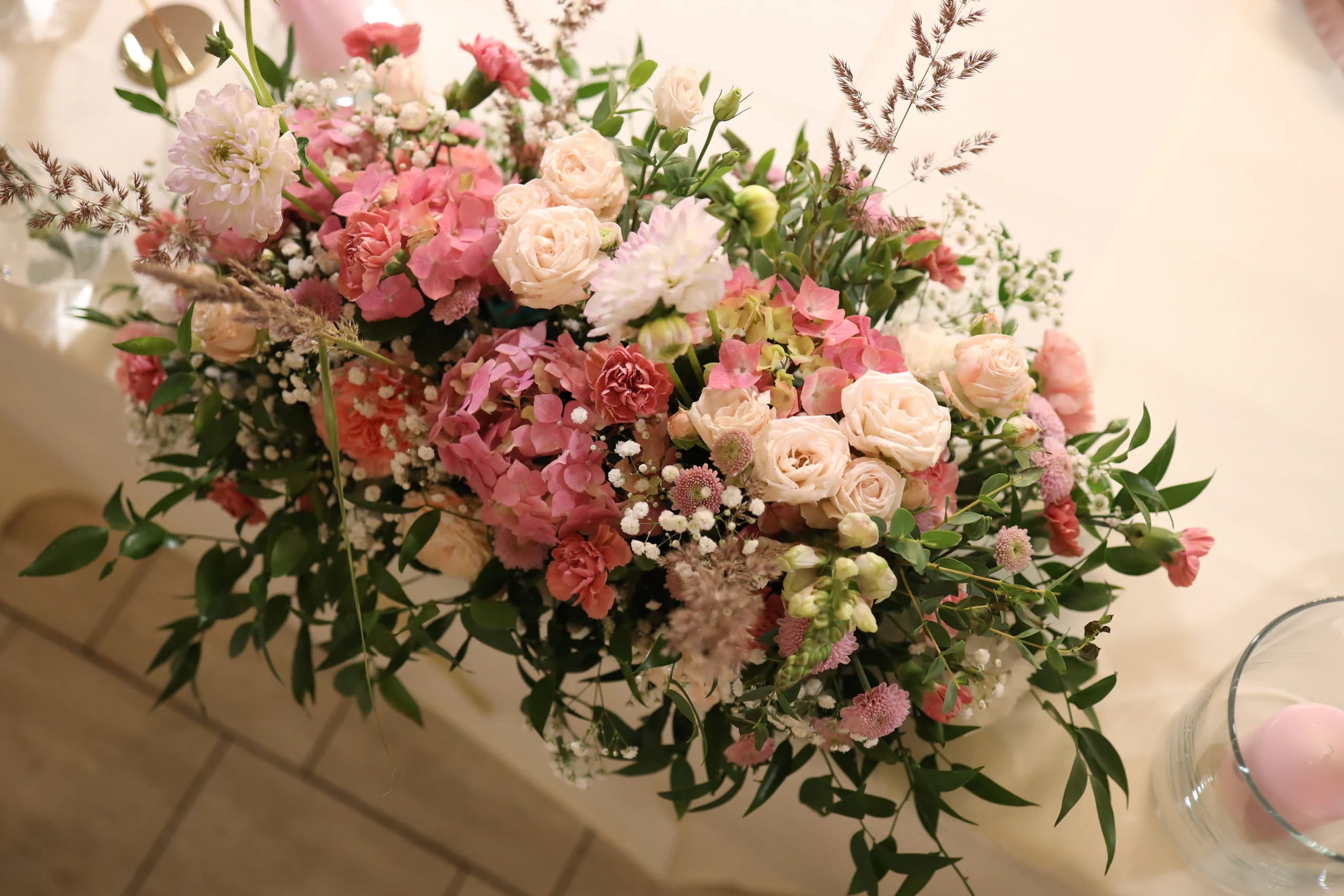 Low composition from above: pink hydrangea, cream and peach spray roses, pale pink dahlias, carnations, gypsophila and grass heads