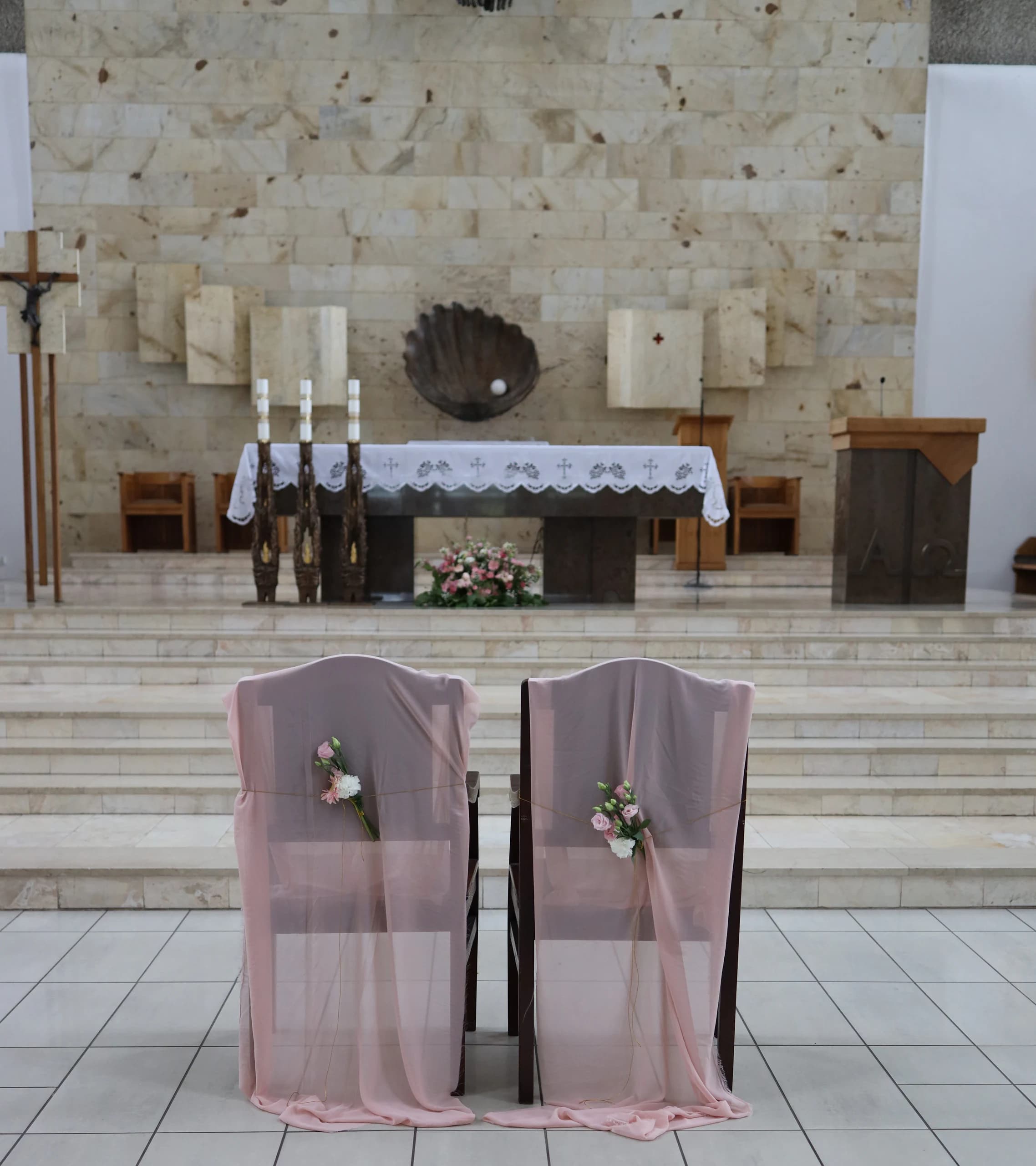 Two chairs of the bride and groom from behind, covered with translucent pink fabric, with small bouquets, altar steps and altar in front of them