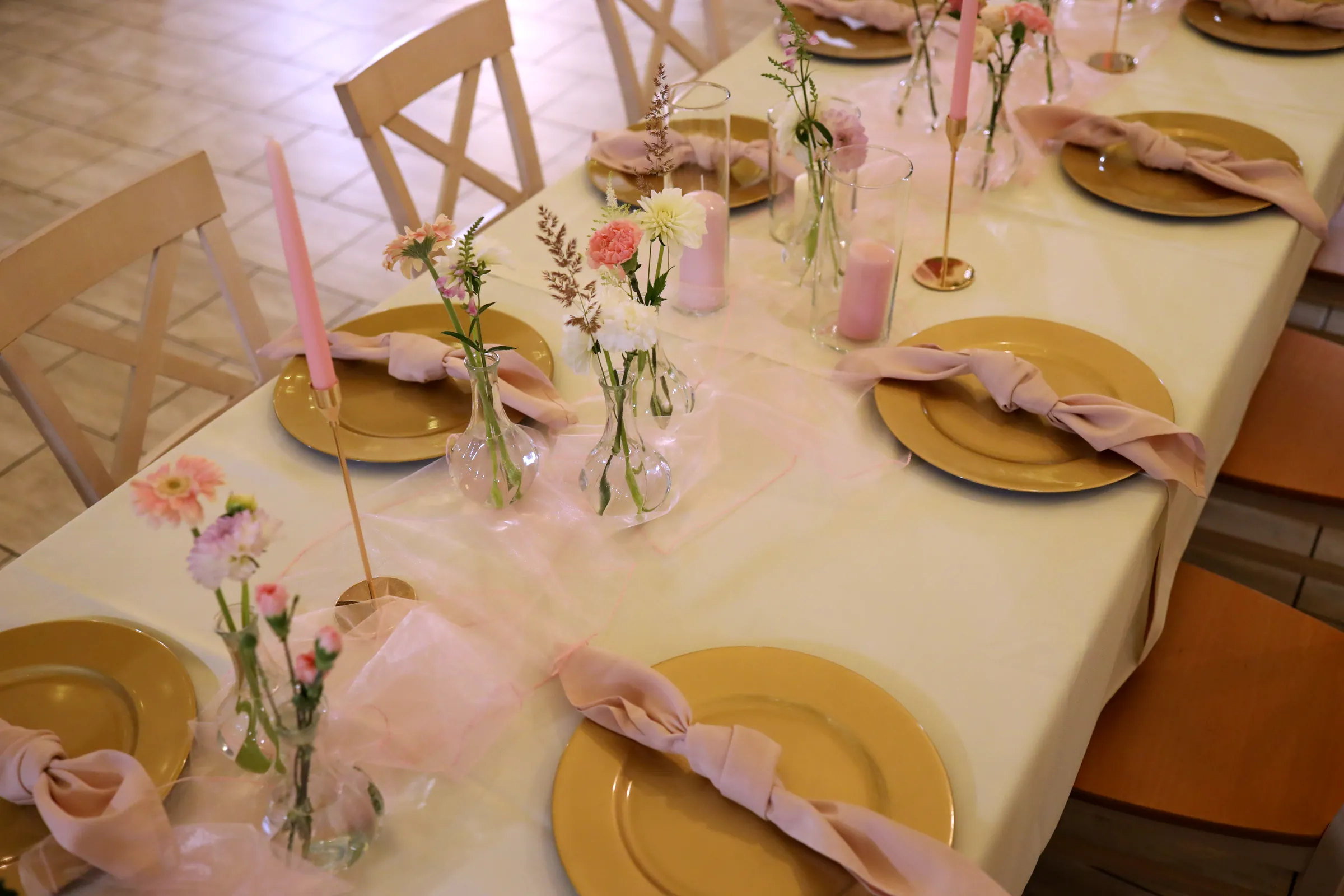 Gold charger plates with powder pink napkins, light pink tulle and small vases with single flowers seen from above
