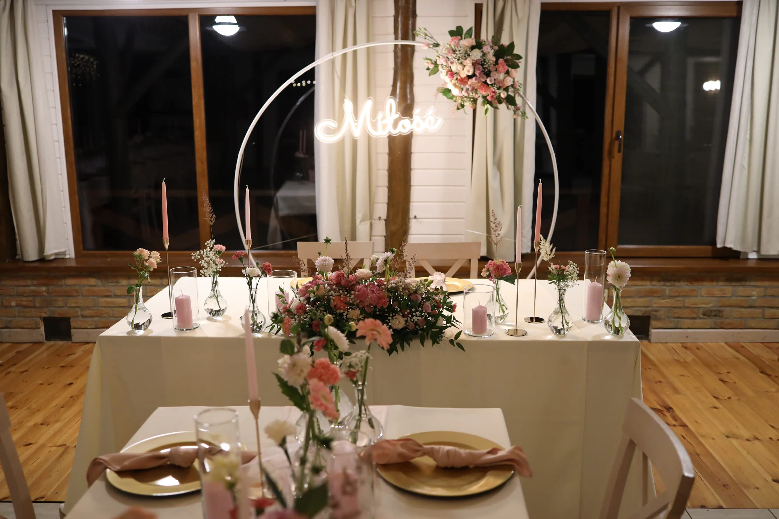 The bride and groom's table in front: a white ring with flowers and the "Love" neon sign, a low composition on the front of the table, pink candles and vases