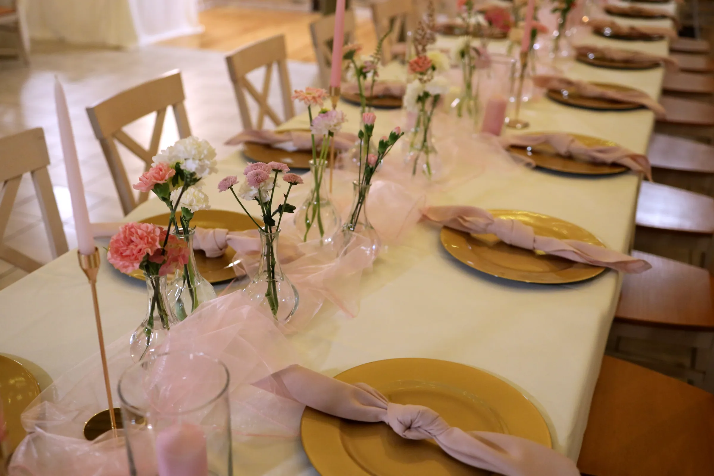 Gold plates with napkins tied in a knot, light pink tulle and vases with carnations on the guests' table
