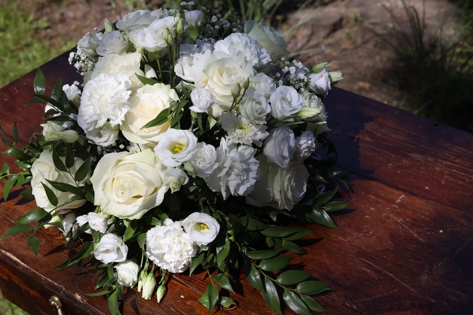 A low, round composition of white roses, carnations, eustoma and gypsophila with ruscus on a dark wooden official's table