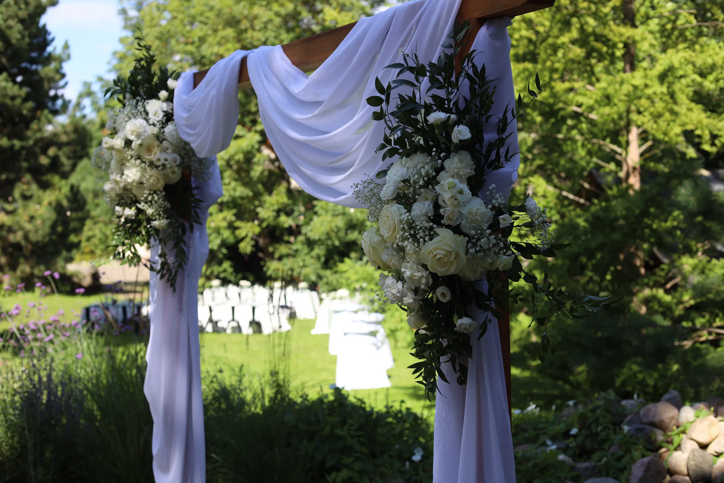 The upper beam of a wooden arch with white fabric and compositions of white roses, carnations, eustoma and gypsophila with ruscus in the corners