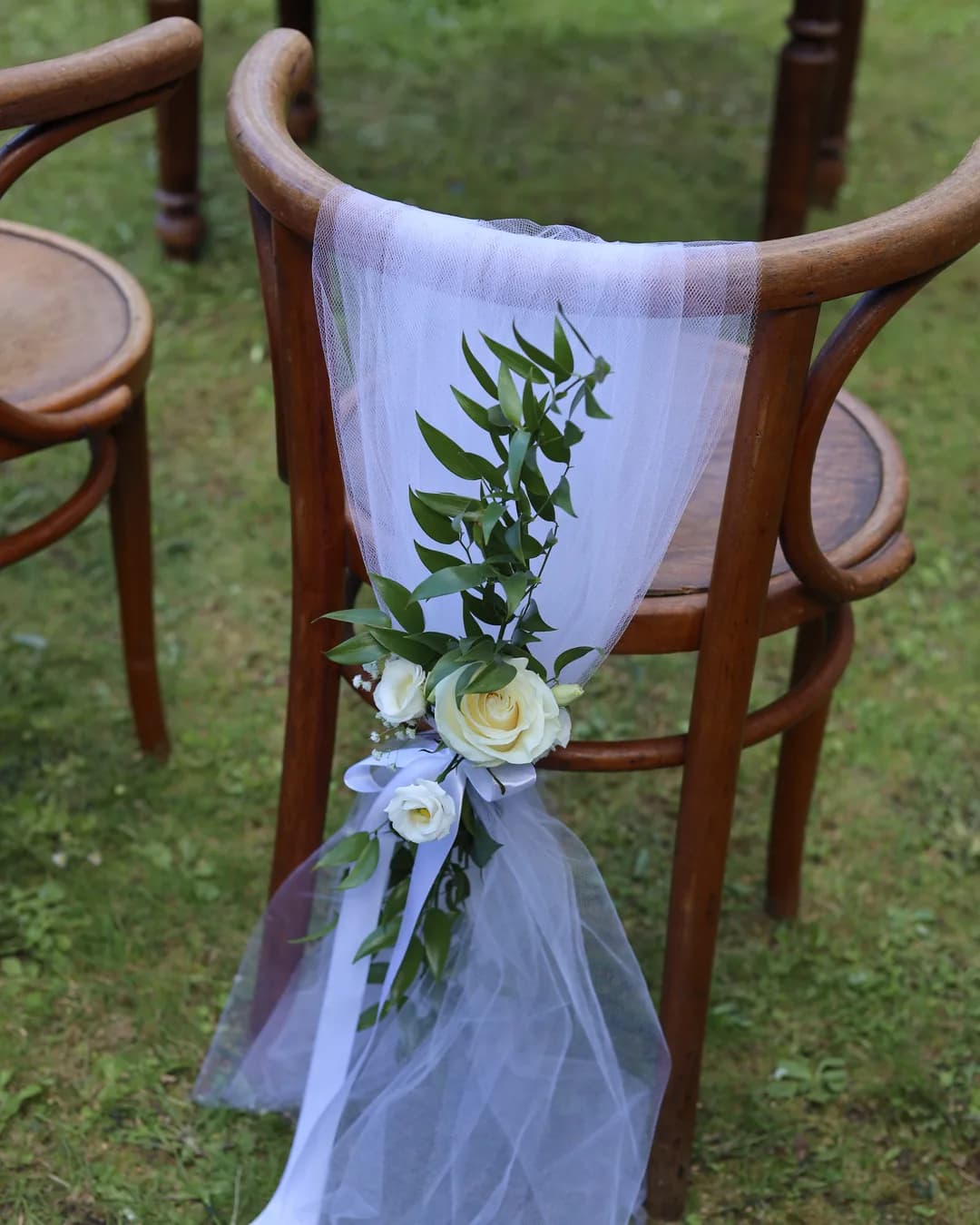 A bent wooden chair for the bride and groom decorated with white tulle, white roses, gypsophila, ruscus and a satin bow
